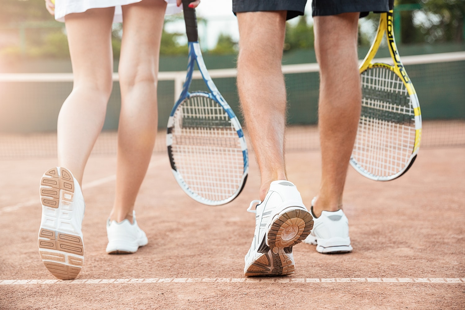 Tennis players walking on clay court, rackets ready.