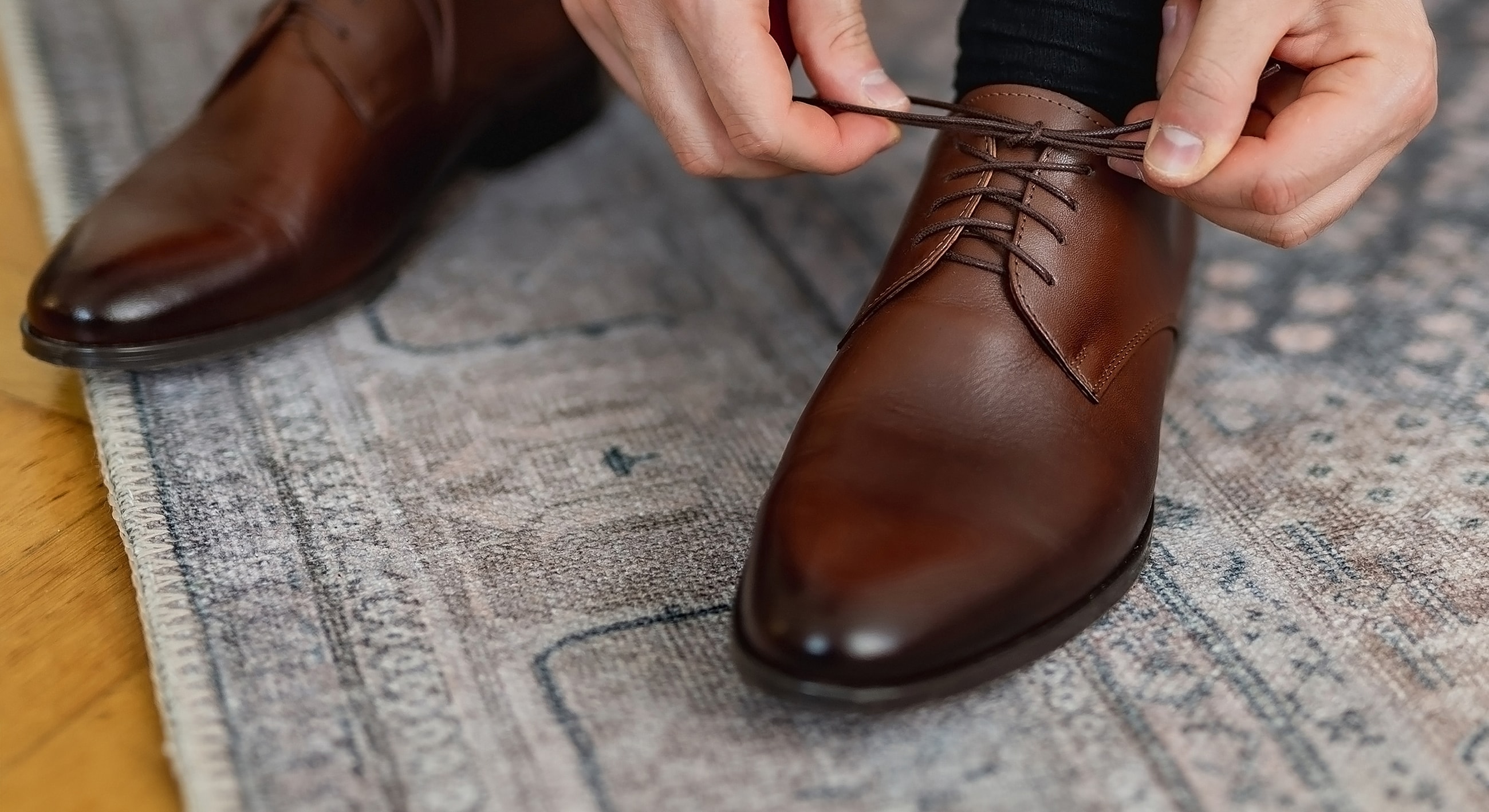 Person tying brown dress shoe laces.