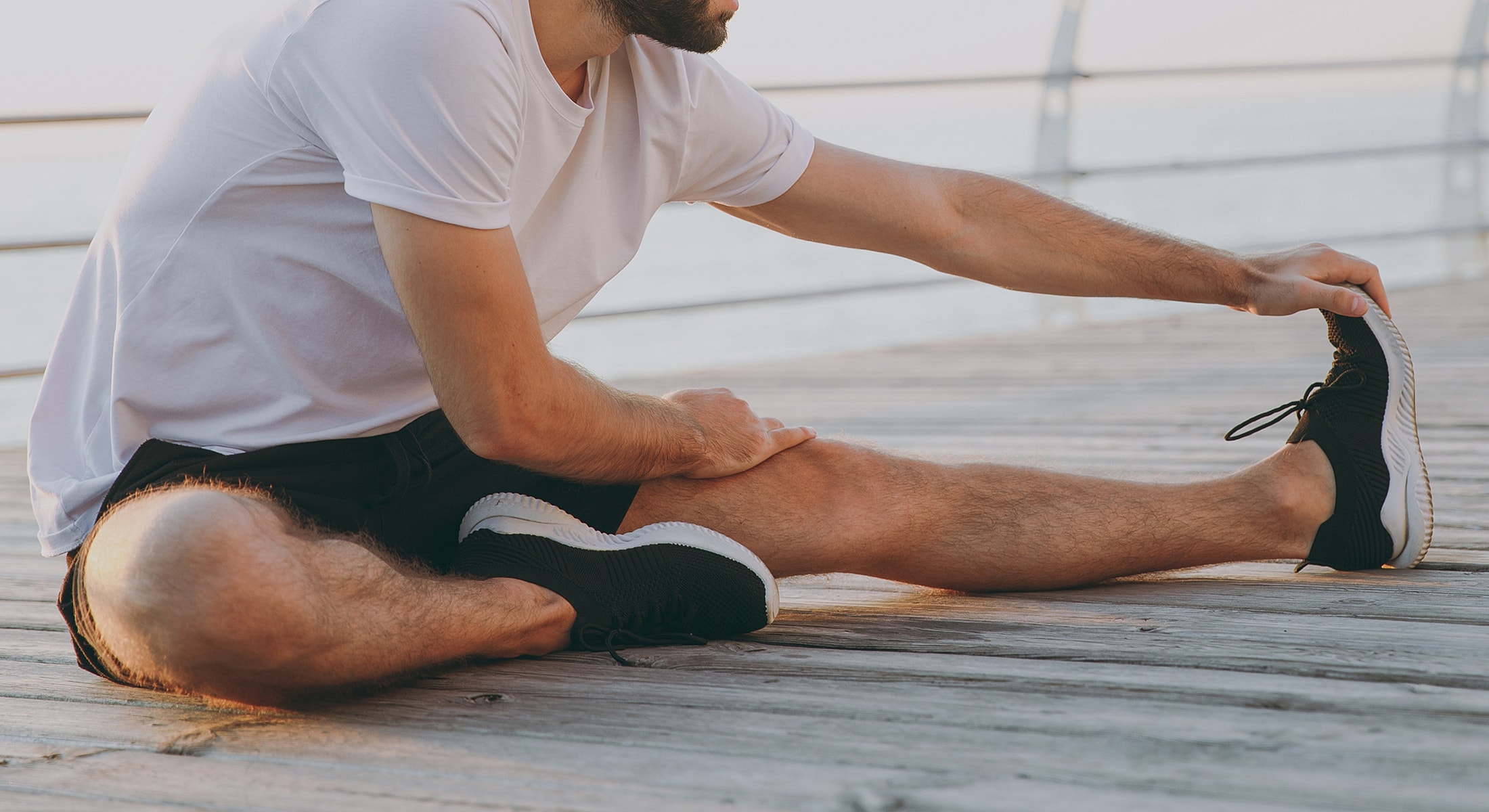 Man stretching on wooden pier by the water.