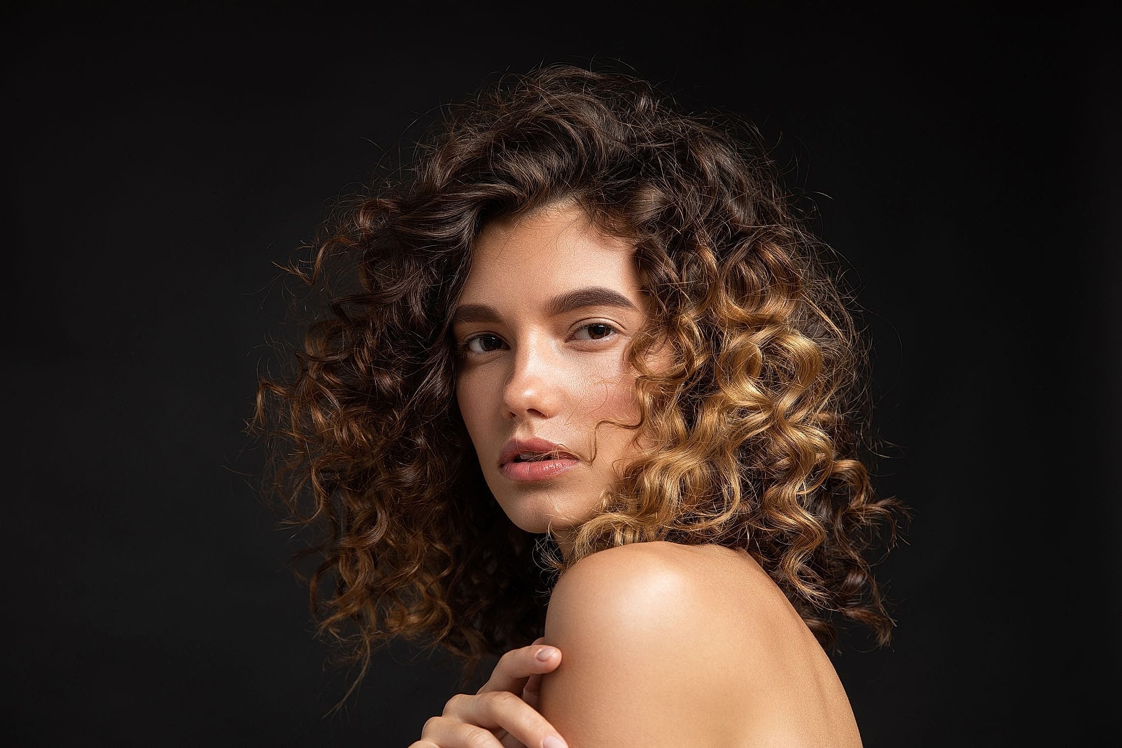 Model with curly hair against a black background.